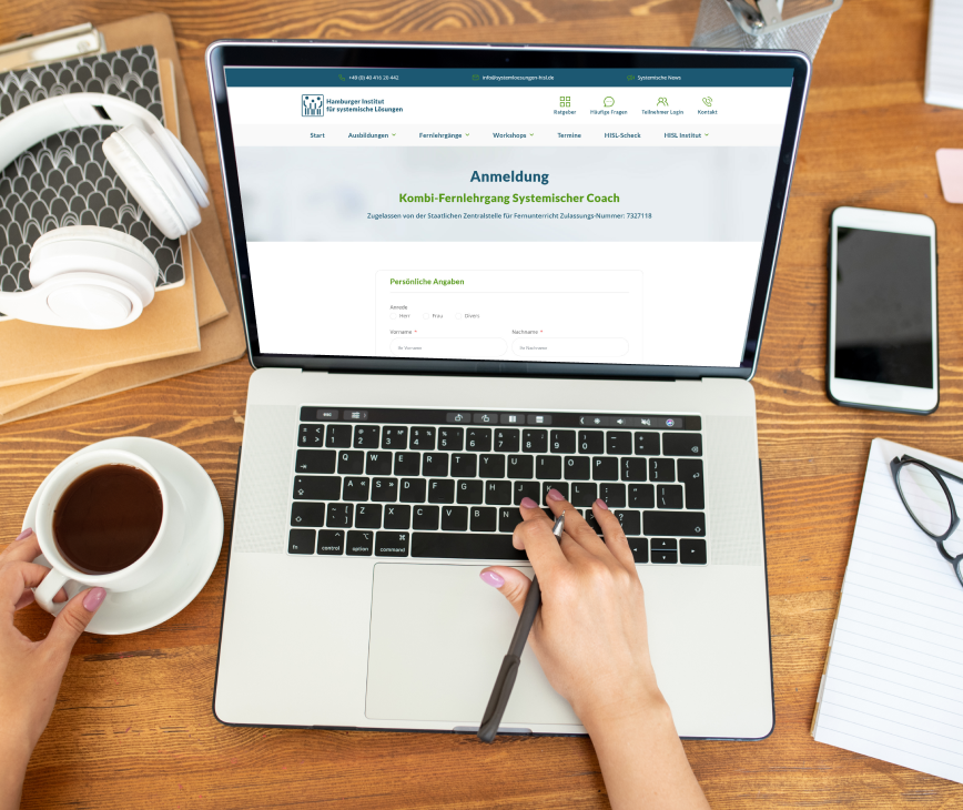 Person, die einen Laptop mit geöffneter Anmeldeseite verwendet, eine Tasse Kaffee hält und von Kopfhörern, einem Smartphone und einem Notizbuch umgeben ist.