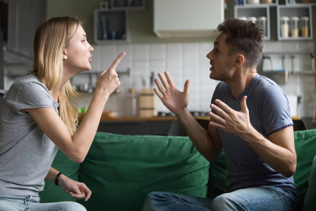 Paar streitet sich auf dem Sofa, beide wirken emotional und reden gestikulierend miteinander.