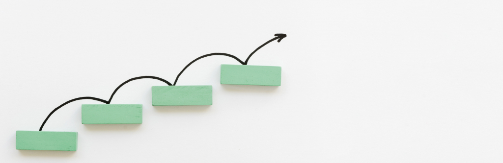 Vier grüne rechteckige Blöcke sind in aufsteigender Reihenfolge angeordnet, über denen jeweils ein schwarzer Pfeil in einer geschwungenen Linie nach oben zeigt, was Wachstum oder Fortschritt bedeutet.