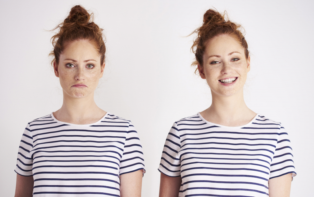 Zwei rothaarige Frauen in gestreiften Hemden, eine links mit einem Stirnrunzeln und eine rechts mit einem Lächeln, stehen vor einem schlichten weißen Hintergrund.