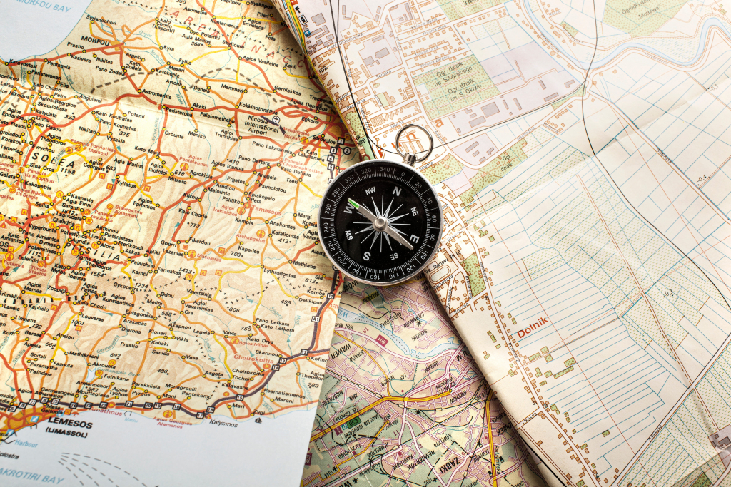 Ein schwarzer Kompass, der auf mehrere ungefaltete Papierkarten mit Straßen, Städten und geografischen Details gelegt wird.